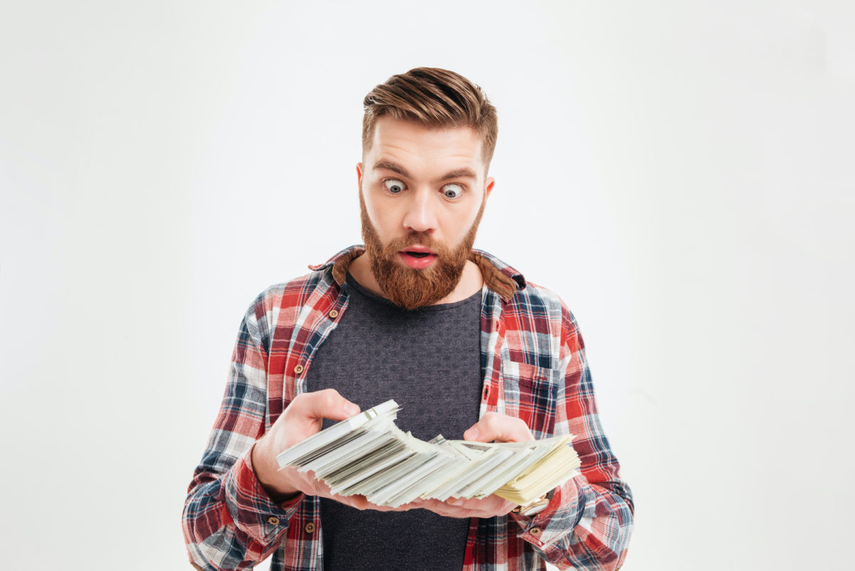 Excited bearded man in plaid shirt looking at money banknotes